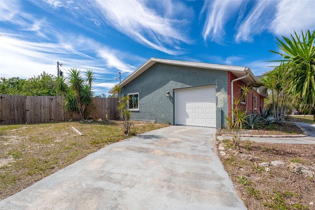 view of side of property with a garage, concrete driveway, fence, and stucco siding