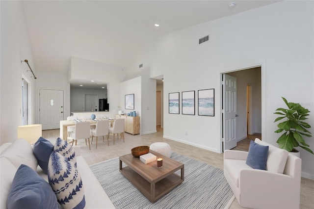 living room with a high ceiling, light wood-style flooring, visible vents, and baseboards