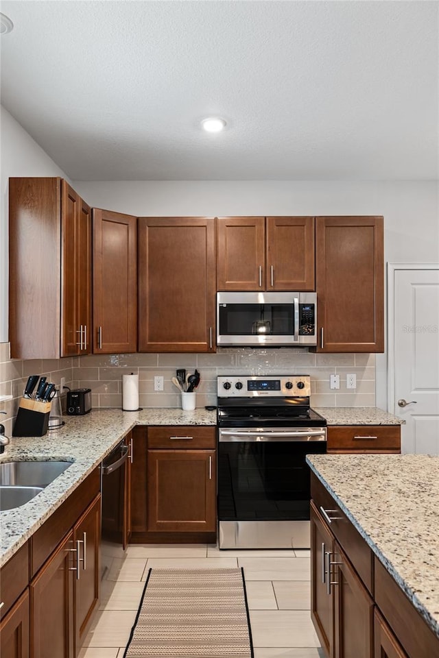 kitchen with light stone countertops, appliances with stainless steel finishes, decorative backsplash, and a sink