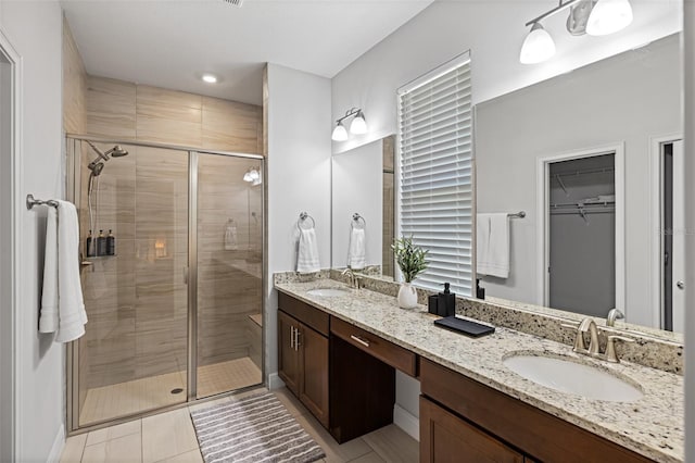 bathroom featuring double vanity, a shower stall, a spacious closet, and a sink