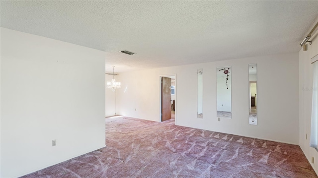 spare room featuring carpet floors, a textured ceiling, visible vents, and a notable chandelier