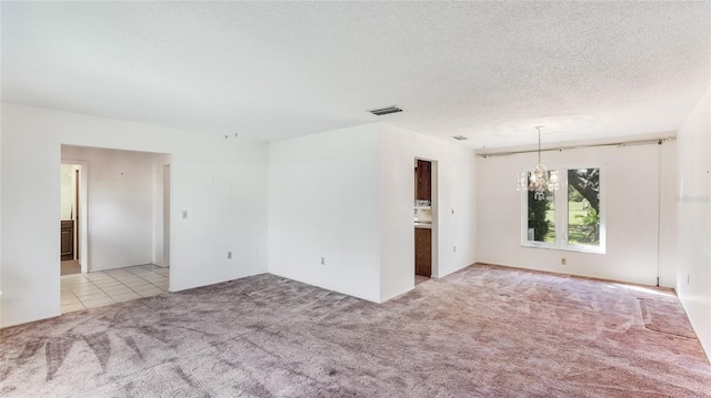 carpeted spare room with visible vents, a textured ceiling, and an inviting chandelier