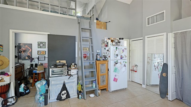 kitchen featuring visible vents, a high ceiling, tile patterned flooring, and freestanding refrigerator