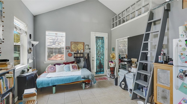 bedroom with light tile patterned flooring, freestanding refrigerator, and high vaulted ceiling