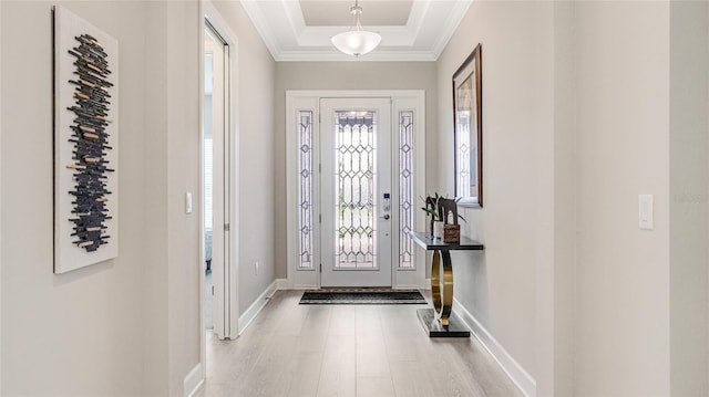 entryway featuring baseboards, a tray ceiling, light wood finished floors, and crown molding