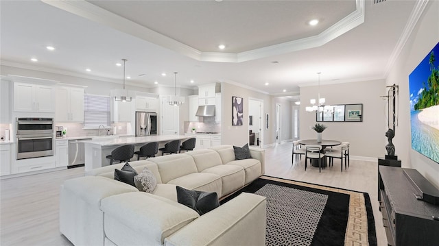 living room with recessed lighting, ornamental molding, light wood finished floors, a raised ceiling, and an inviting chandelier