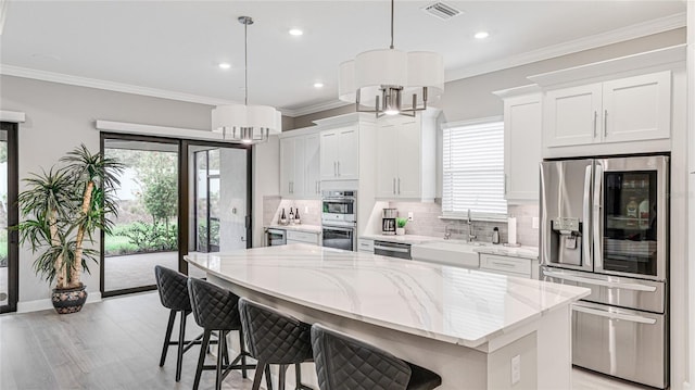 kitchen featuring visible vents, a kitchen island, ornamental molding, stainless steel appliances, and a sink