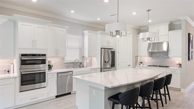 kitchen featuring crown molding, appliances with stainless steel finishes, a sink, under cabinet range hood, and a kitchen bar