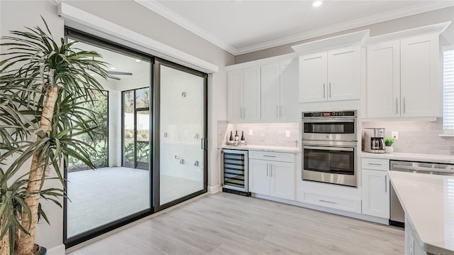 kitchen featuring wine cooler, ornamental molding, stainless steel appliances, light countertops, and white cabinetry