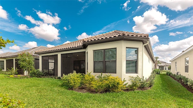 back of property featuring a sunroom, a tile roof, stucco siding, and a yard