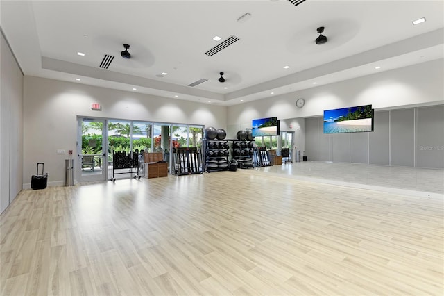 workout area featuring a high ceiling, a raised ceiling, recessed lighting, and light wood-style floors