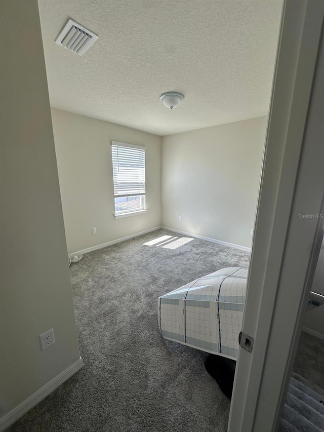 carpeted spare room featuring a textured ceiling, visible vents, and baseboards