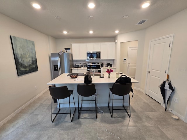 kitchen with a breakfast bar, a center island with sink, white cabinets, and stainless steel appliances