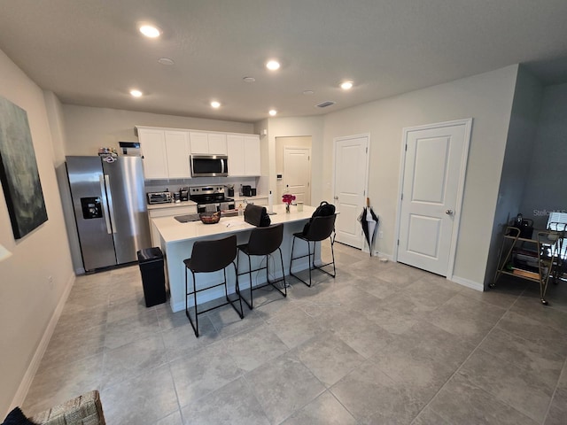 kitchen with an island with sink, a kitchen breakfast bar, stainless steel appliances, white cabinetry, and recessed lighting