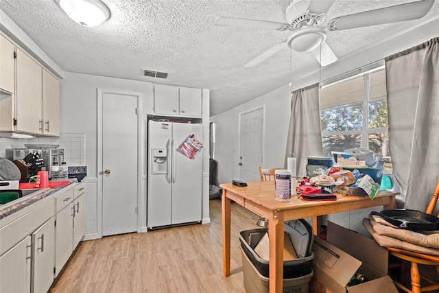 kitchen with light wood finished floors, visible vents, decorative backsplash, ceiling fan, and white fridge with ice dispenser