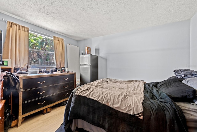 bedroom featuring a textured ceiling, light wood-type flooring, and freestanding refrigerator