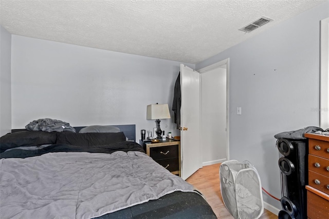 bedroom featuring baseboards, visible vents, a textured ceiling, and light wood finished floors