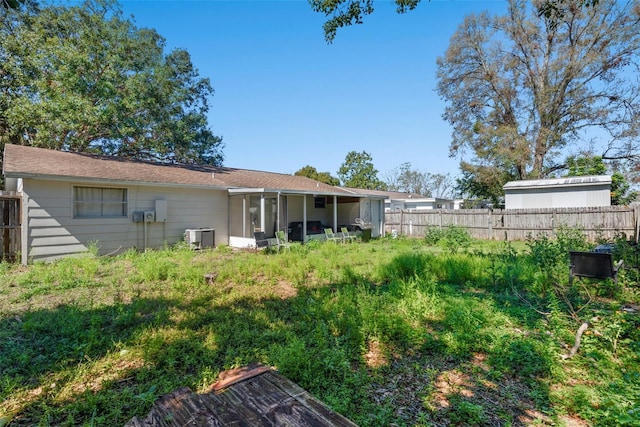 rear view of house with central AC, a fenced backyard, and a sunroom