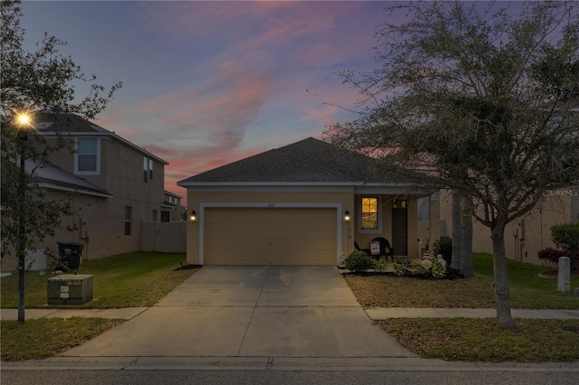 view of front facade with concrete driveway, stucco siding, a lawn, a garage, and a shingled roof