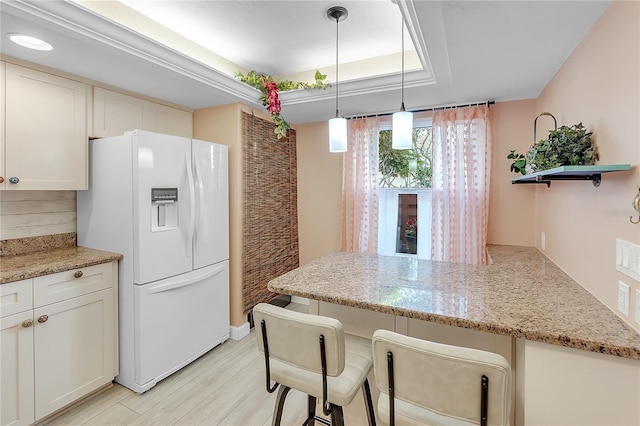 kitchen featuring a raised ceiling, white cabinets, white fridge with ice dispenser, light wood-type flooring, and a peninsula