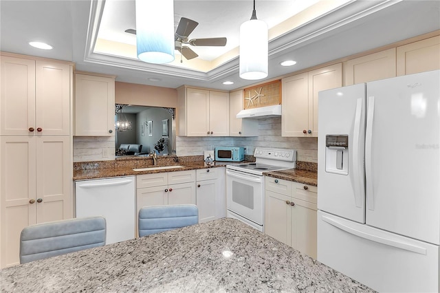 kitchen with white appliances, tasteful backsplash, a raised ceiling, under cabinet range hood, and a sink