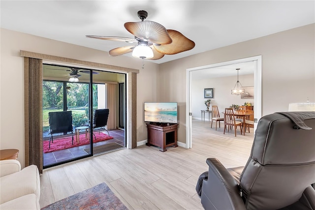 living room with ceiling fan with notable chandelier, light wood-type flooring, and baseboards