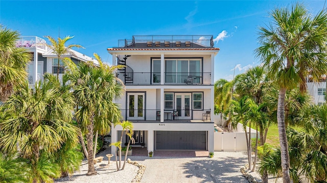 coastal inspired home with a balcony, stucco siding, a gate, and french doors