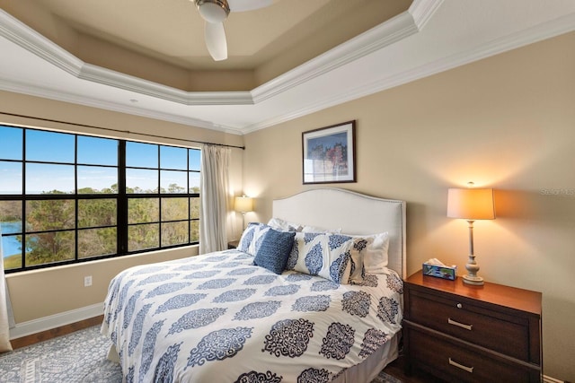 bedroom featuring a raised ceiling, ornamental molding, wood finished floors, baseboards, and ceiling fan