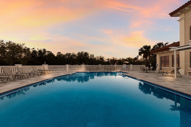 pool at dusk featuring a patio, a community pool, and fence