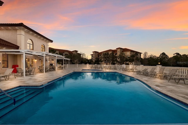 pool at dusk with a patio, a community pool, and fence
