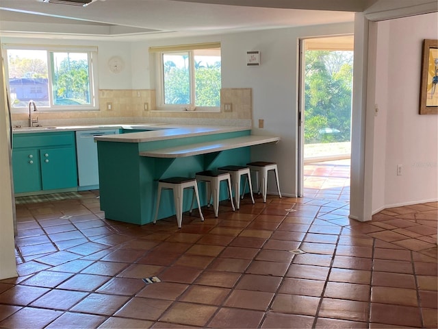 kitchen featuring a peninsula, tasteful backsplash, white dishwasher, and a sink