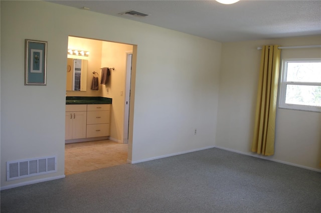 unfurnished bedroom featuring light tile patterned flooring, visible vents, connected bathroom, and light colored carpet