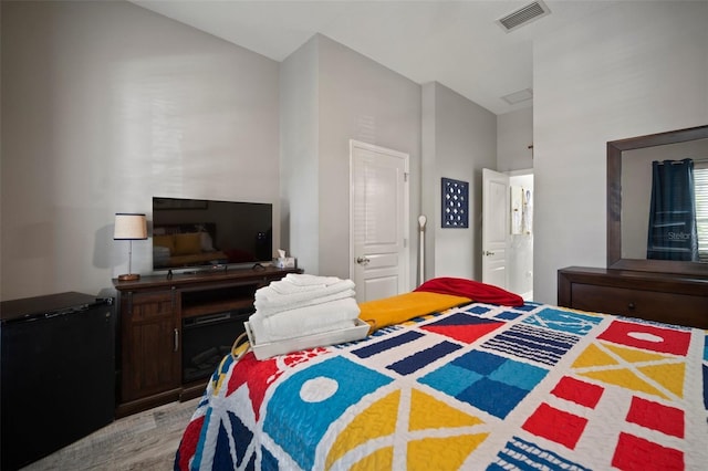 bedroom with vaulted ceiling, fridge, visible vents, and light wood finished floors