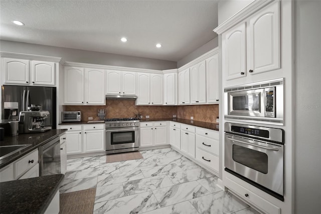 kitchen with backsplash, under cabinet range hood, appliances with stainless steel finishes, white cabinets, and marble finish floor