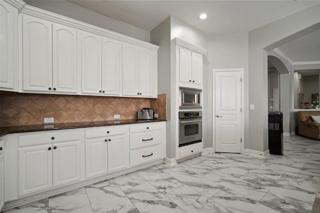 kitchen with marble finish floor, tasteful backsplash, arched walkways, appliances with stainless steel finishes, and white cabinets