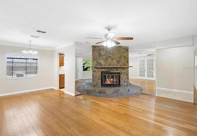 unfurnished living room with baseboards, wood finished floors, crown molding, a stone fireplace, and ceiling fan with notable chandelier