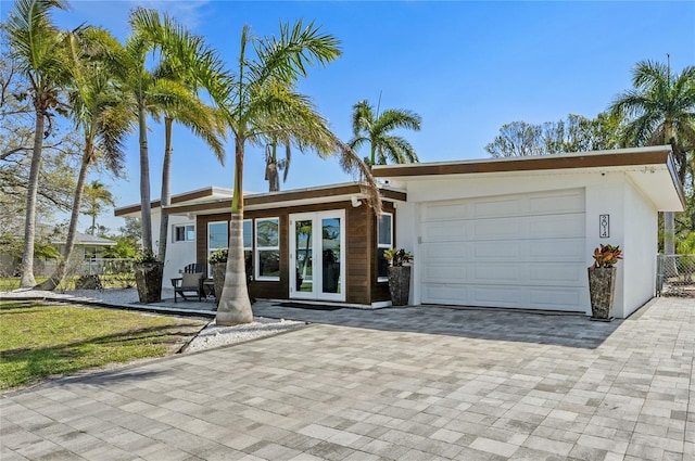 view of front of home featuring decorative driveway, french doors, stucco siding, an attached garage, and fence