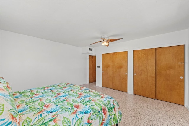 bedroom with light speckled floor, a ceiling fan, visible vents, and two closets