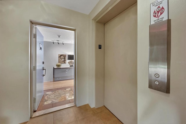 hall featuring light tile patterned floors, a textured ceiling, and elevator