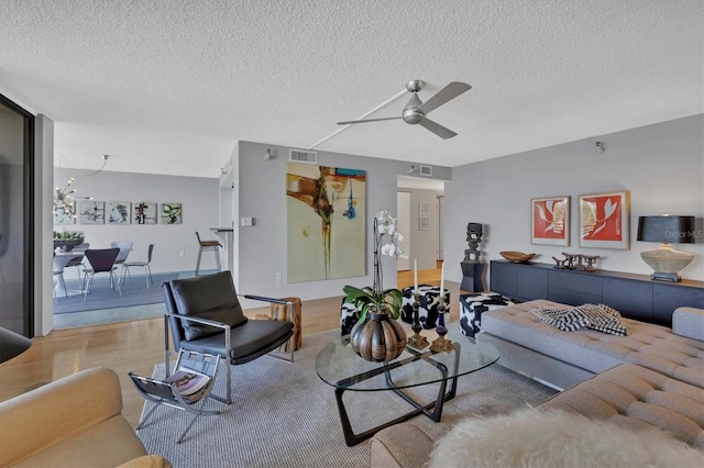 living area with a ceiling fan, visible vents, a textured ceiling, and wood finished floors