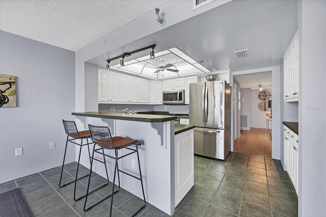 kitchen with appliances with stainless steel finishes, dark countertops, visible vents, and a breakfast bar