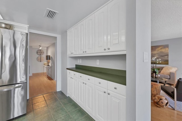 kitchen with visible vents, dark countertops, freestanding refrigerator, and white cabinetry