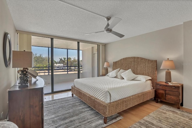 bedroom with access to exterior, a ceiling fan, expansive windows, a textured ceiling, and wood finished floors