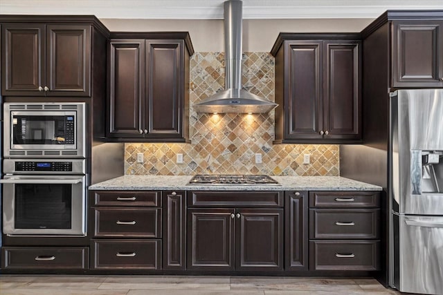 kitchen with light stone countertops, wall chimney range hood, ornamental molding, and stainless steel appliances