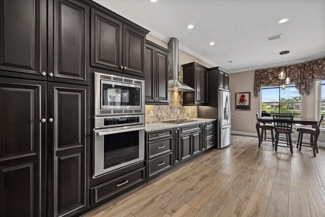 kitchen with wall chimney exhaust hood, light wood-style flooring, ornamental molding, stainless steel appliances, and backsplash