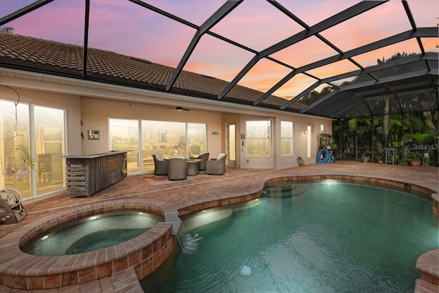 pool at dusk featuring a patio area, a pool with connected hot tub, and glass enclosure