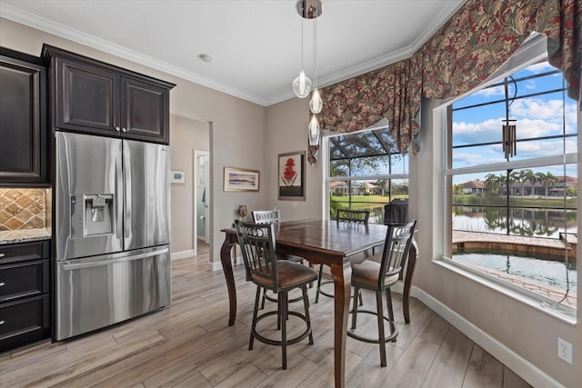 dining space featuring ornamental molding, a water view, light wood-style flooring, and baseboards