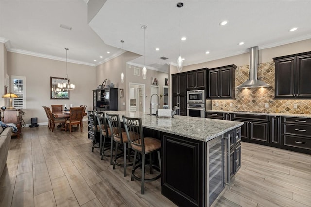 kitchen featuring stainless steel appliances, light wood-style flooring, decorative backsplash, wall chimney range hood, and beverage cooler