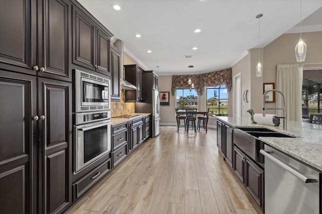 kitchen featuring appliances with stainless steel finishes, light stone counters, decorative light fixtures, light wood-style floors, and a sink