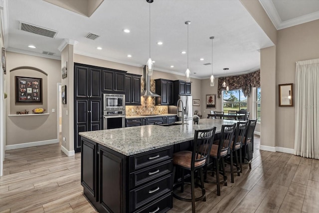 kitchen featuring wall chimney exhaust hood, visible vents, stainless steel appliances, and dark cabinetry